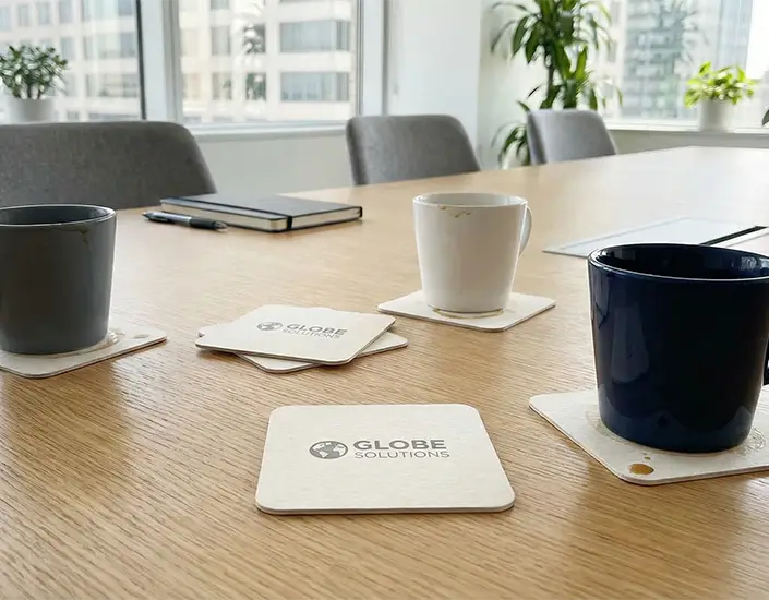 Branded pulpboard coasters with coffee mugs on a modern conference table in a corporate office.