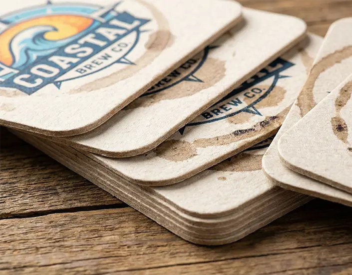Stack of custom printed pulpboard coasters showing moisture absorption and branded artwork.