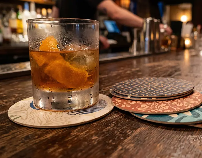 Close-up of cocktail on pulpboard coaster with stack of custom printed coasters on bar table.