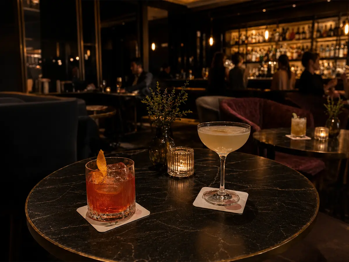 Cocktails served on custom coasters in an upscale bar setting with warm lighting and guests in the background.
