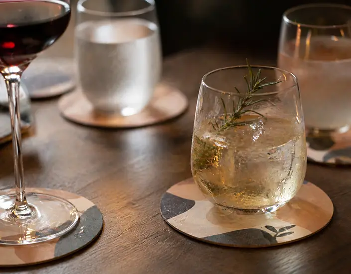 Close-up of cocktails placed on custom printed coasters highlighting branding and drink presentation in a restaurant setting.