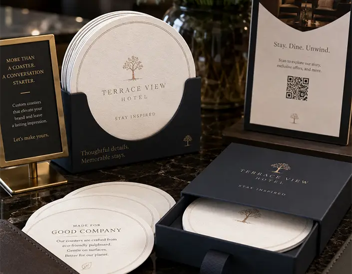 Premium hotel coaster display with branded pulpboard coasters, a gift box, signage, and a QR code card on a counter.