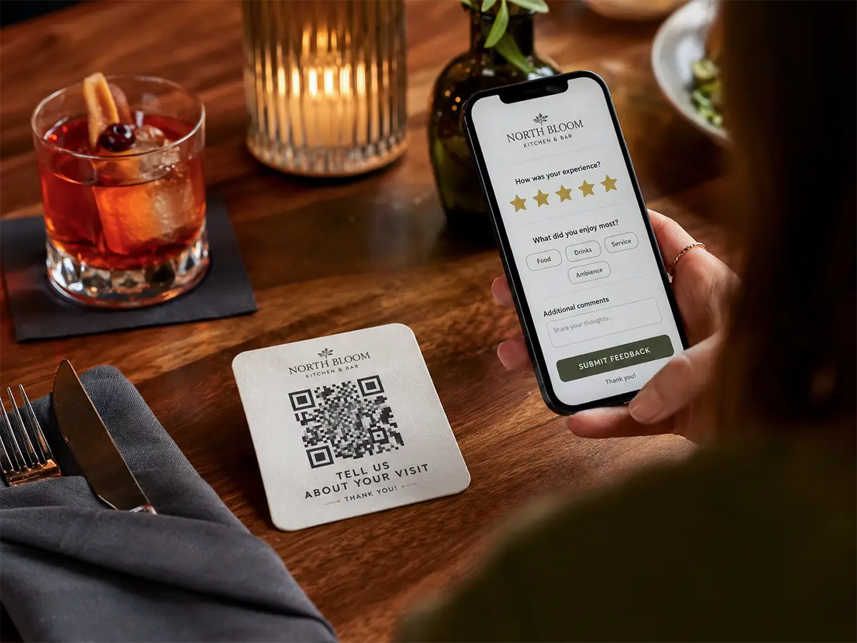 Customer scanning a QR code coaster at a restaurant table to open a feedback survey on their phone.