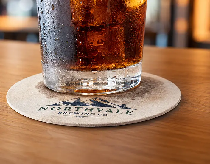 Cold drink with condensation on a custom printed pulpboard coaster absorbing moisture.