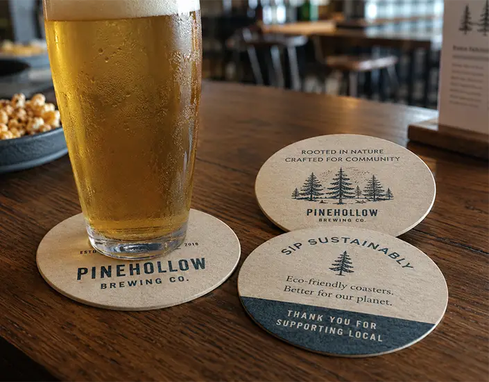 Eco friendly pulpboard beer coasters with custom brewery branding on a wooden bar table.