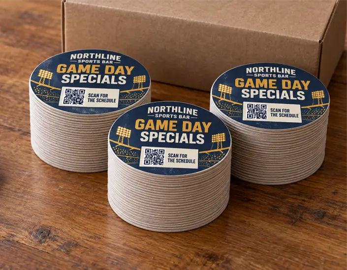 Three stacks of custom sports bar coasters promoting game day specials, with QR codes for the schedule.